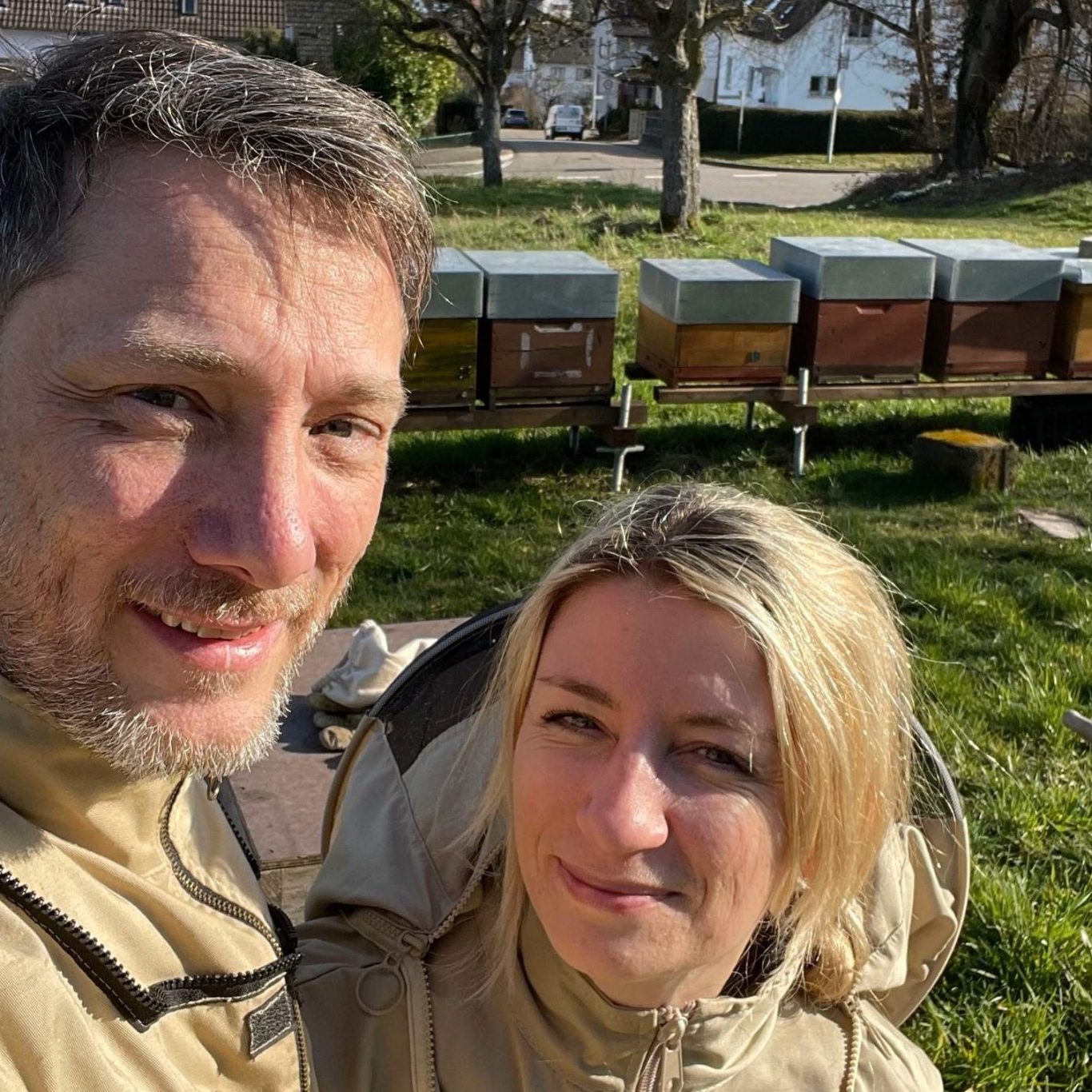 Melanie und Elmar mit Bienenvölkern im Hintergrund auf einer Wiese.